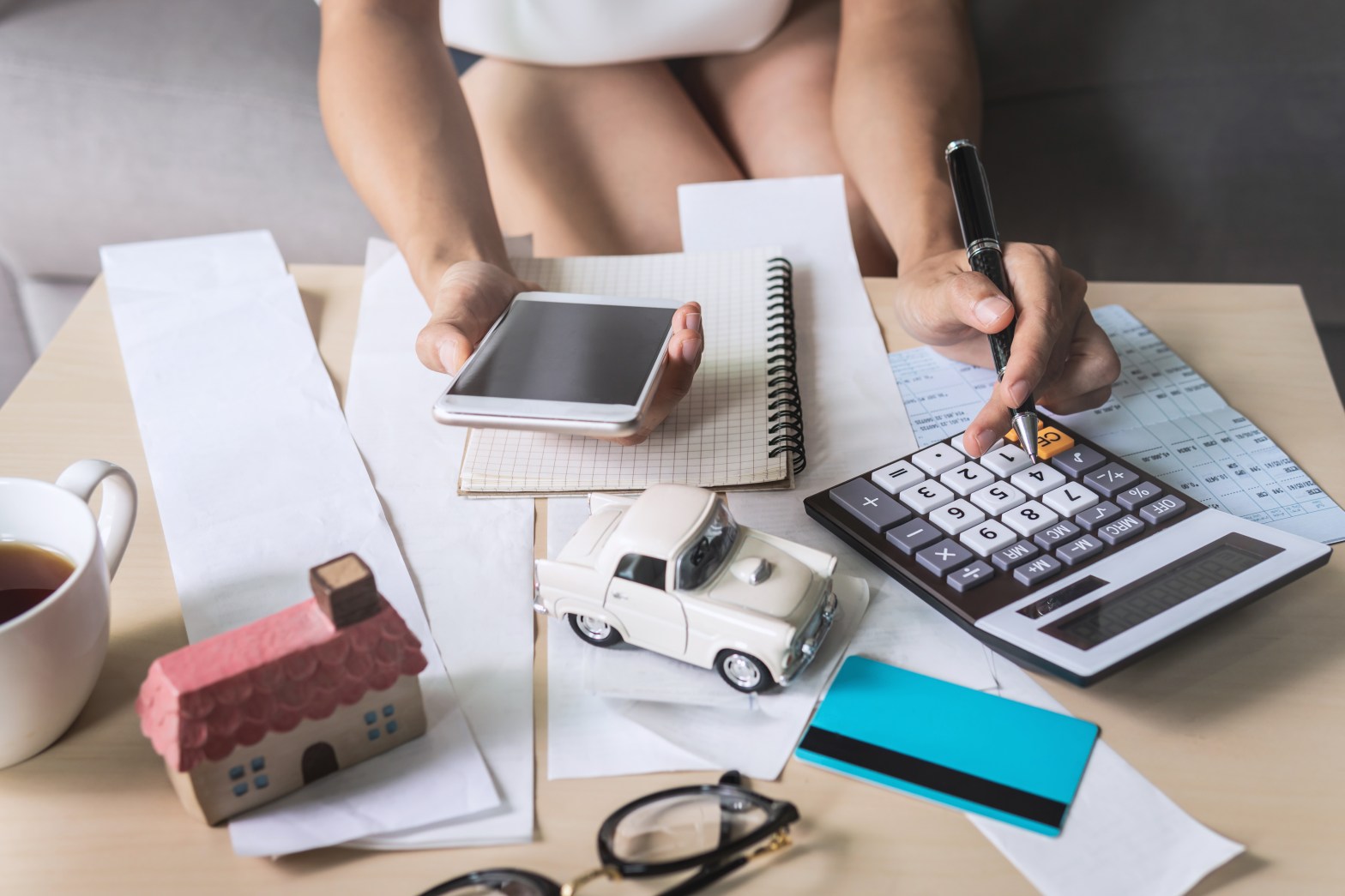 Young woman using smart phone and checking bills, taxes, bank account balance and calculating expenses in the living room at home